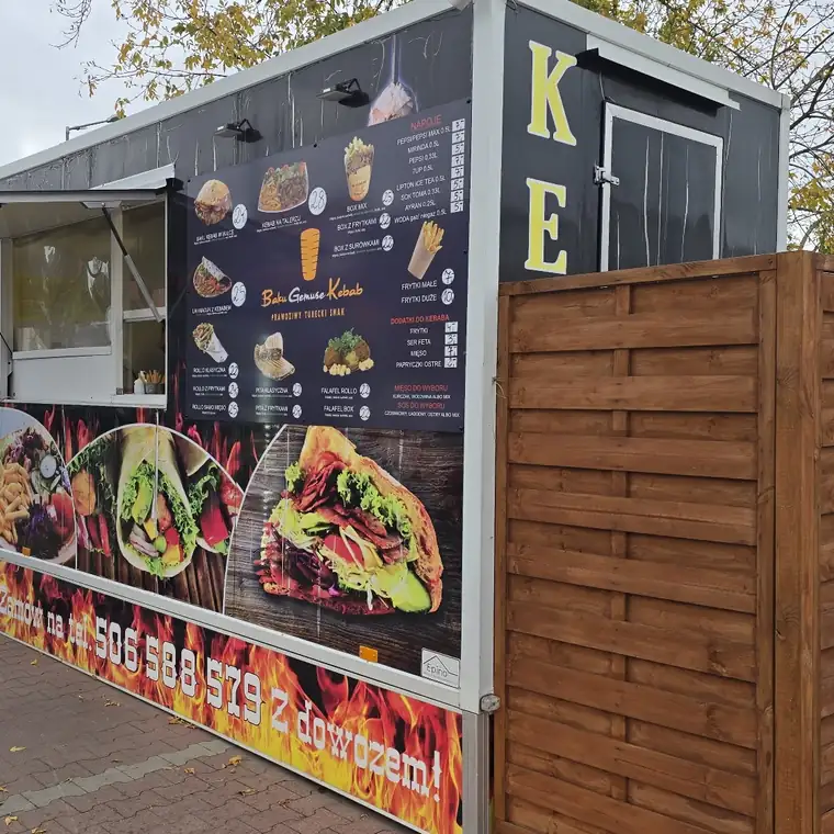 Budka z kebabem i tablicą menu przy drewnianym płocie